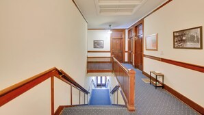A hotel hallway with a wooden staircase, carpeted floors, and framed pictures on the walls. - Epic Silver Valley Basecamp: Steps to Dtwn Fun! (Wallace)
