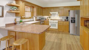 A modern kitchen with wooden cabinets, granite countertops, a stainless steel refrigerator, and a built-in oven. - Fish, Hike & Relax: Heber Springs Family Home (Heber Springs)