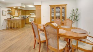 A dining area with a wooden table and chairs, a kitchen in the background, and a cabinet with glass doors. - Fish, Hike & Relax: Heber Springs Family Home (Heber Springs)