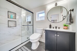 Une salle de bain moderne avec une douche à parois de verre, des toilettes, un lavabo avec un miroir et une plante en pot.