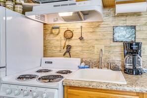 A kitchen with a white stove, a granite countertop, a sink, and various kitchen utensils hanging on the wall. - Walkable & Convenient Main Street Studio in Delphi (Delphi)