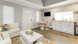 Eine moderne Küche mit weißen Schränken, ein Essbereich mit weißem Tisch und Stühlen sowie ein Wohnzimmer mit weißem Sofa und farbenfrohem Teppich.