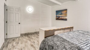 A bedroom with a herringbone-patterned wooden floor, a white door, a bedside table, a bed with a floral-patterned bedspread, and a painting of a sunset on the wall. - 1 Mi to Main St Eats! Single-Level Red Bluff Home (Red Bluff)