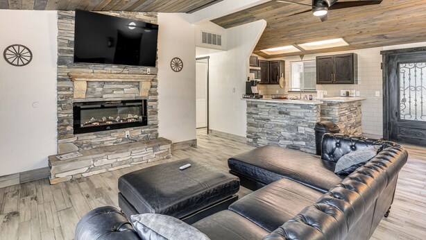 A modern living room with a stone fireplace, leather sofa, and a flat-screen TV mounted on the wall. - 1 Mi to Main St Eats! Single-Level Red Bluff Home (Red Bluff)