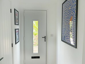 Eine weiße Tür mit kleinem Fenster, einem an der Wand befestigten Lichtschalter und zwei gerahmten Bildern an der linken Wand.
