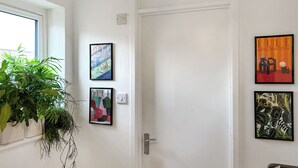 Una puerta blanca con tres cuadros en la pared, una planta en maceta y una ventana con vistas.