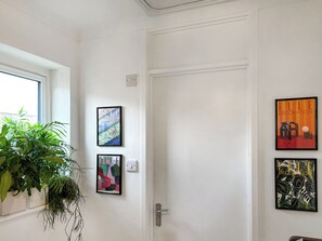 Eine weiße Tür mit drei gerahmten Bildern an der Wand, einem Blumentopf und einem Fenster mit Ausblick.