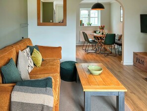 A living room with a sofa, a coffee table, and a dining area with chairs and a table. - 3 bedroom accommodation in Newquay (Newquay)