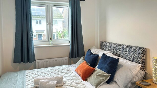 Un dormitorio con cama, una ventana con cortinas, un radiador y una mesita de noche con lámpara.