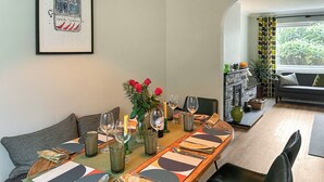 Un comedor con una mesa de madera larga dispuesta para cuatro personas, rodeada de sillas tapizadas en verde.