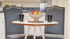 A kitchen with two grey upholstered chairs, a round table with a white top, and a bowl of fruit on a wooden coaster. - Cozy Condo in the Heart of Canmore (Canmore)