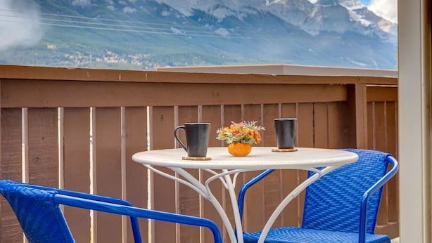 A balcony with a white table, two blue chairs, a vase with flowers, and two black mugs. - Cozy Condo in the Heart of Canmore (Canmore)