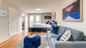 A modern bedroom with a large bed, a gray sofa, and a blue ottoman. - Cozy Condo in the Heart of Canmore (Canmore)