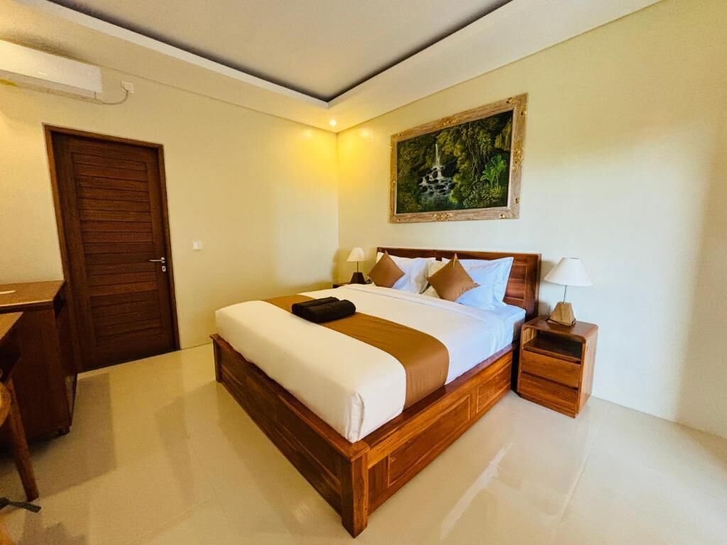 A hotel room with a wooden bed, a desk, a nightstand, and a painting on the wall.