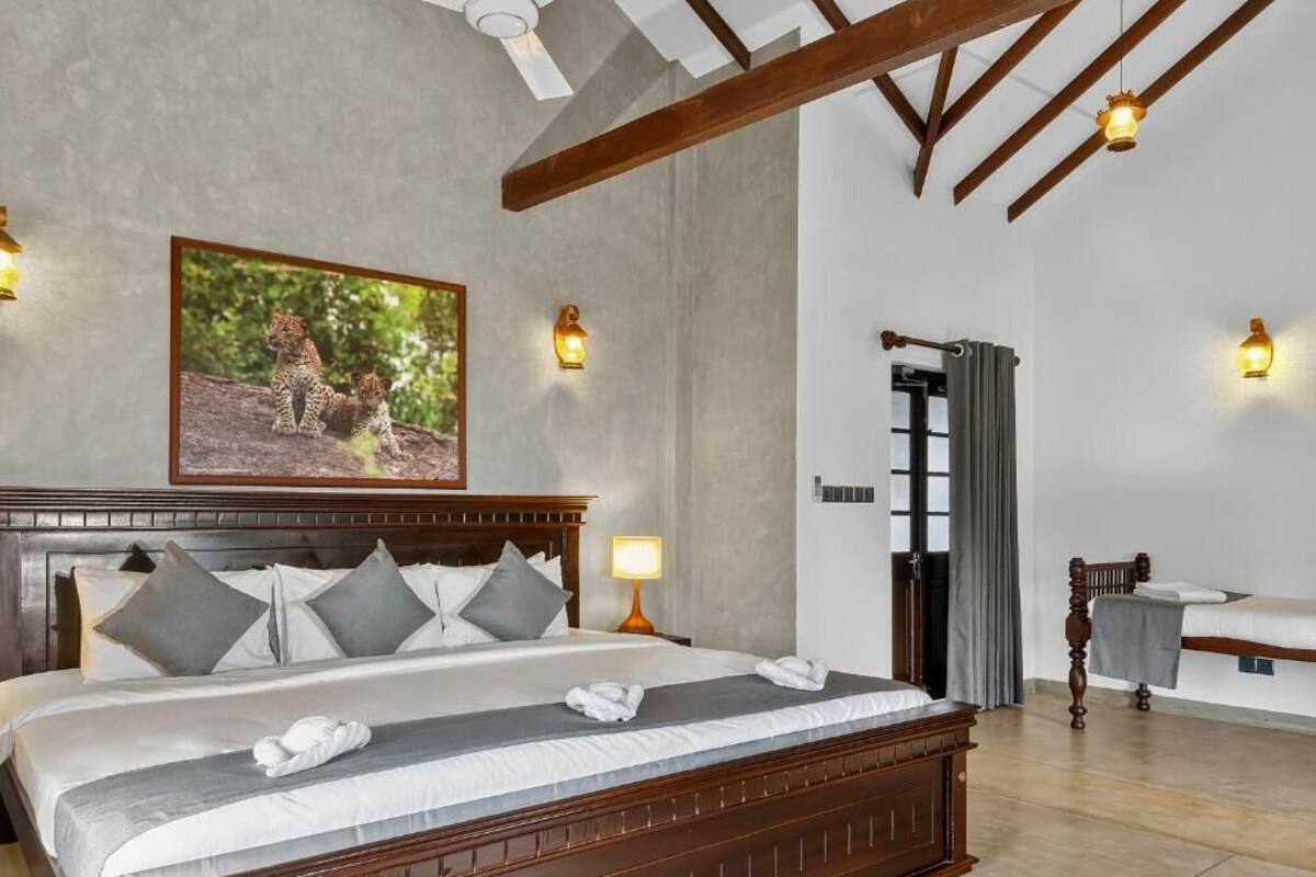 A bedroom with a large bed, a wooden headboard, a painting of leopards, and wall-mounted lights.