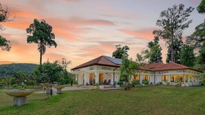 A two-story house with a garden in front, surrounded by trees and hills. - The Tusker's Hideout (Alawwa)