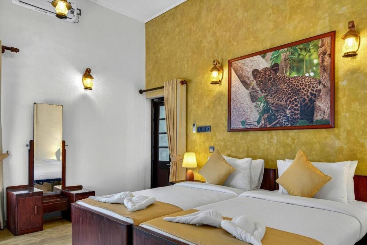 A hotel room with two beds, a large painting of a leopard, and wall-mounted lights.