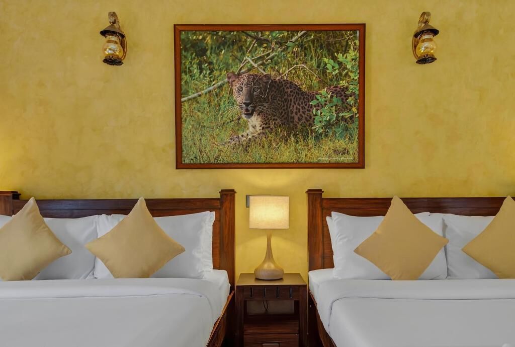 Een hotelkamer met twee bedden, een nachtkastje met een lamp en een ingelijst beeld van een luipaard aan de muur.