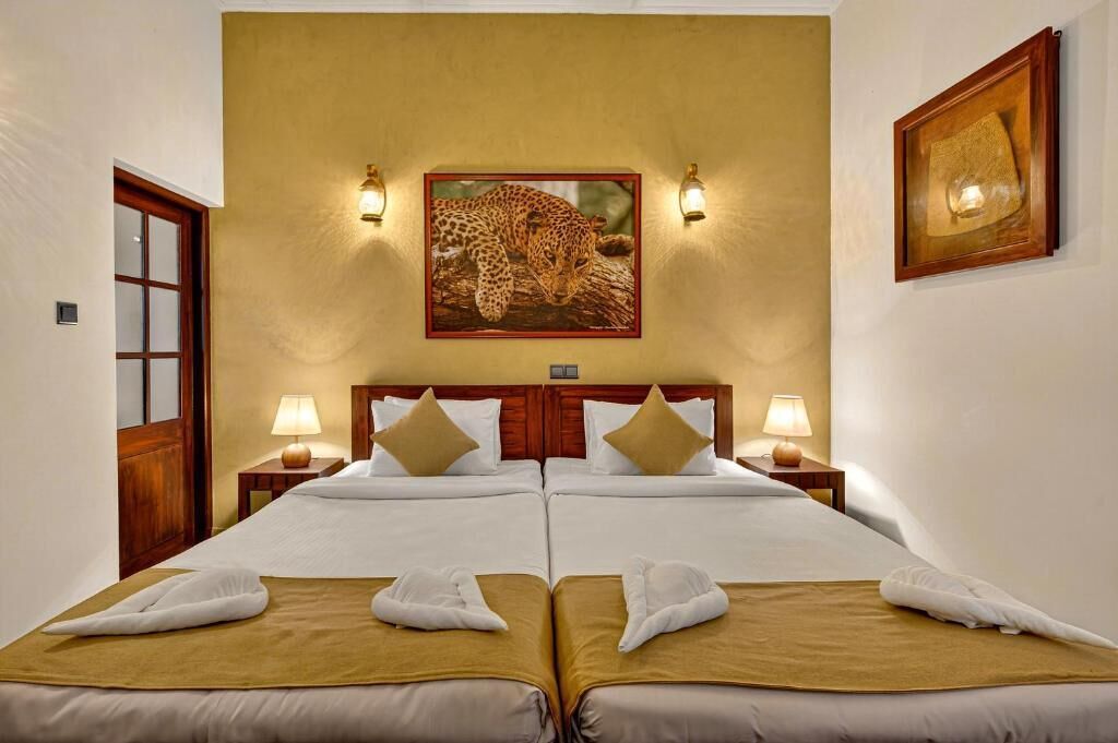 Habitación con cama doble, dos mesitas de noche, un cuadro con estampado de leopardo en la pared y dos lámparas de pared.