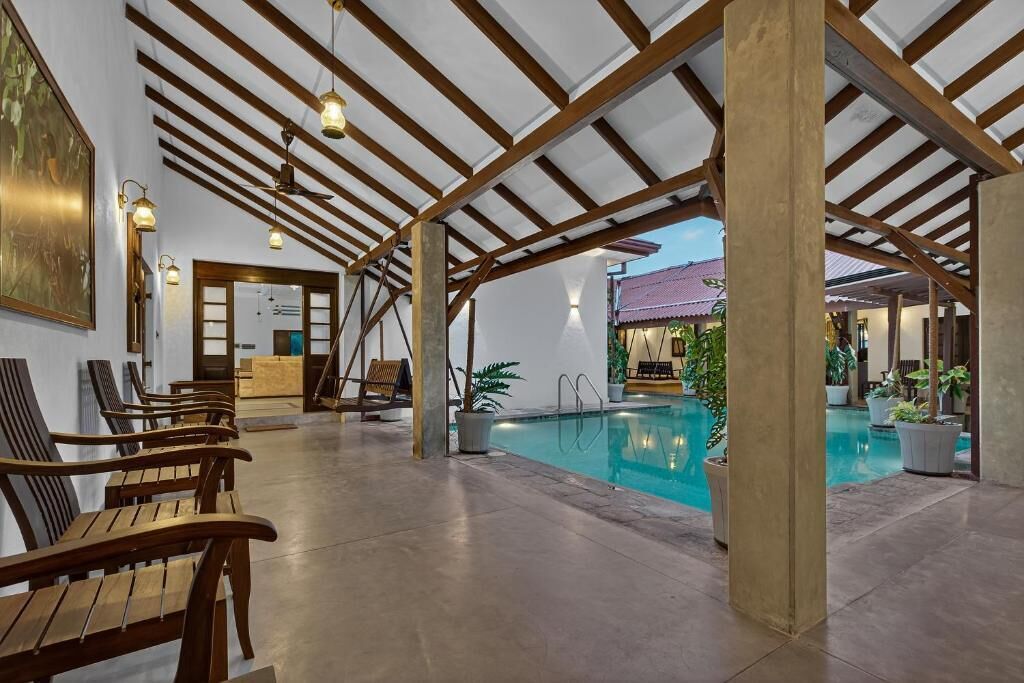 A pool area with wooden benches, a reception desk, and a view of a building with a red roof.