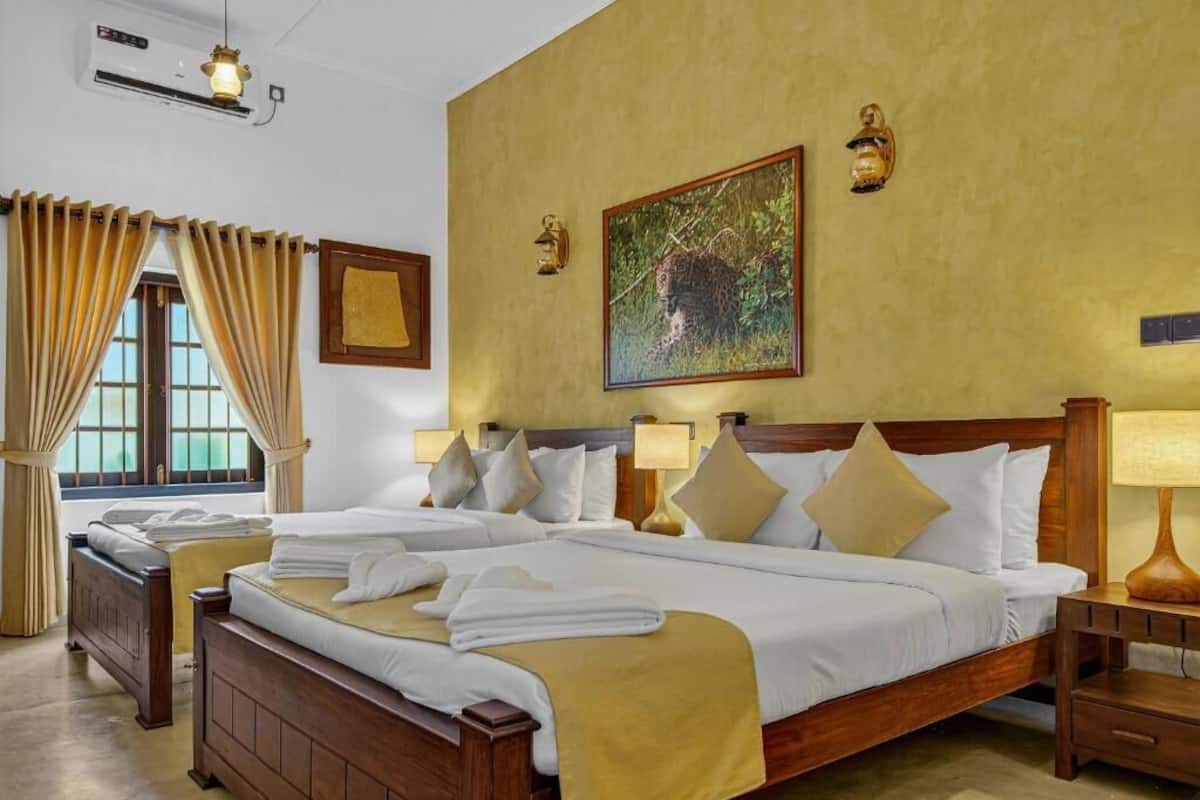 A hotel room with two beds, a large window with curtains, a painting on the wall, and two wall-mounted lamps.