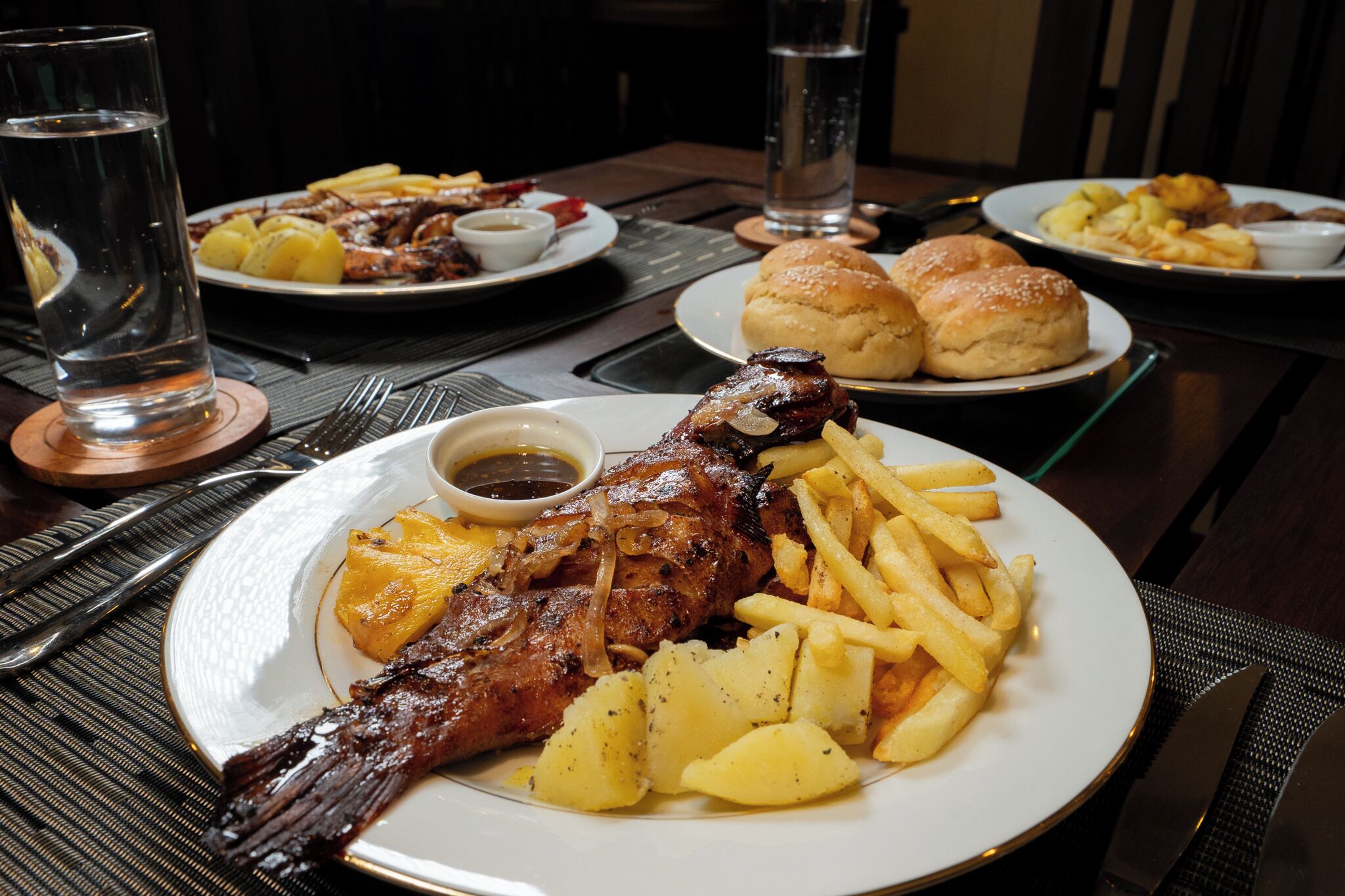 Una mesa de comedor con platos de comida, incluyendo un pollo asado, papas fritas y panecillos.