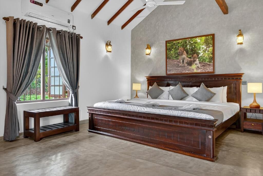 A bedroom with a large bed, wooden headboard, two bedside tables with lamps, a bench, and a window with curtains.
