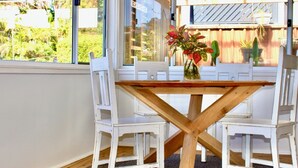 Une table à manger avec un plateau en bois et une structure en croisillons, entourée de chaises blanches. Un vase rempli de fleurs est posé sur la table.