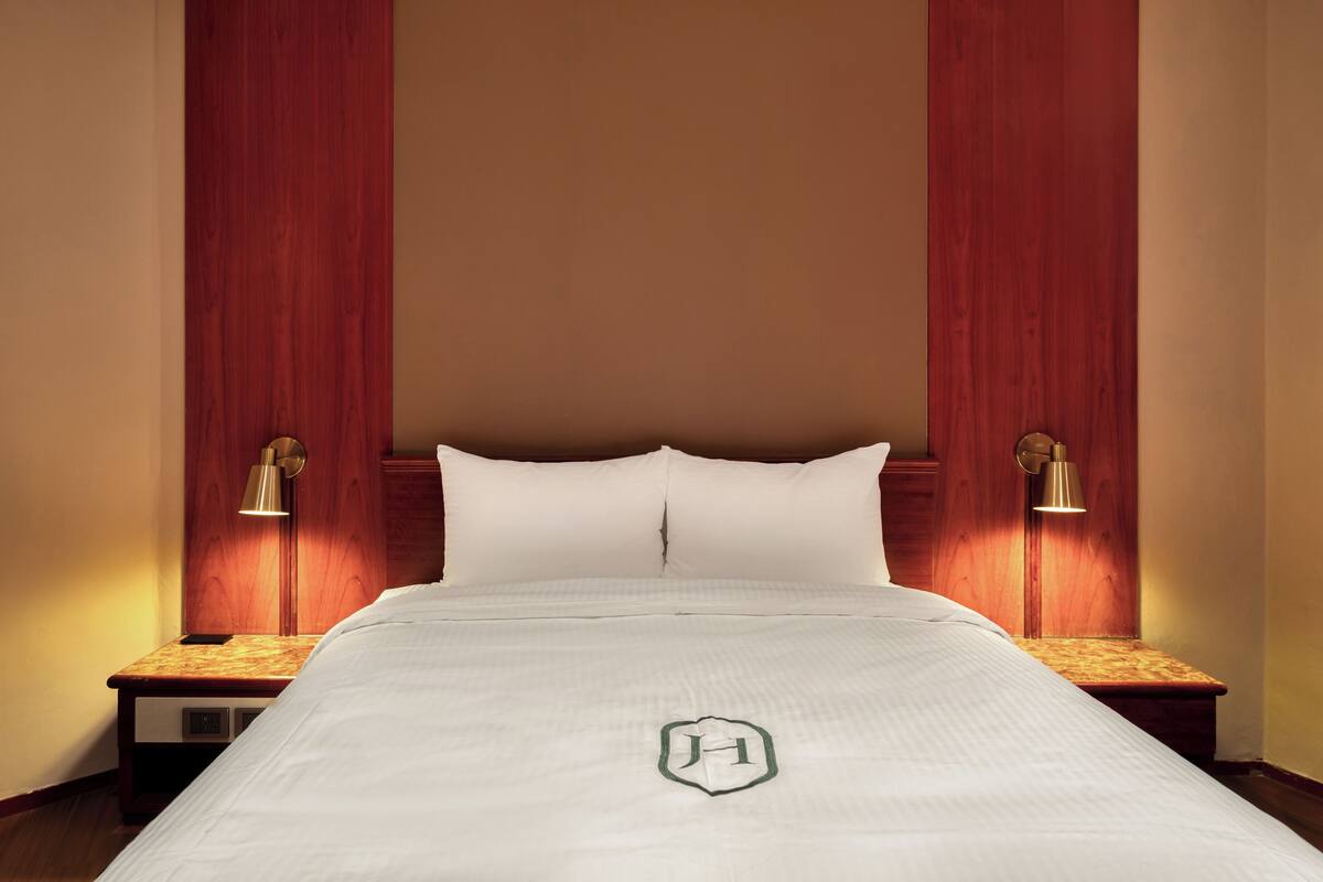A hotel room with a large bed, wooden headboard, two bedside lamps, and a nightstand.