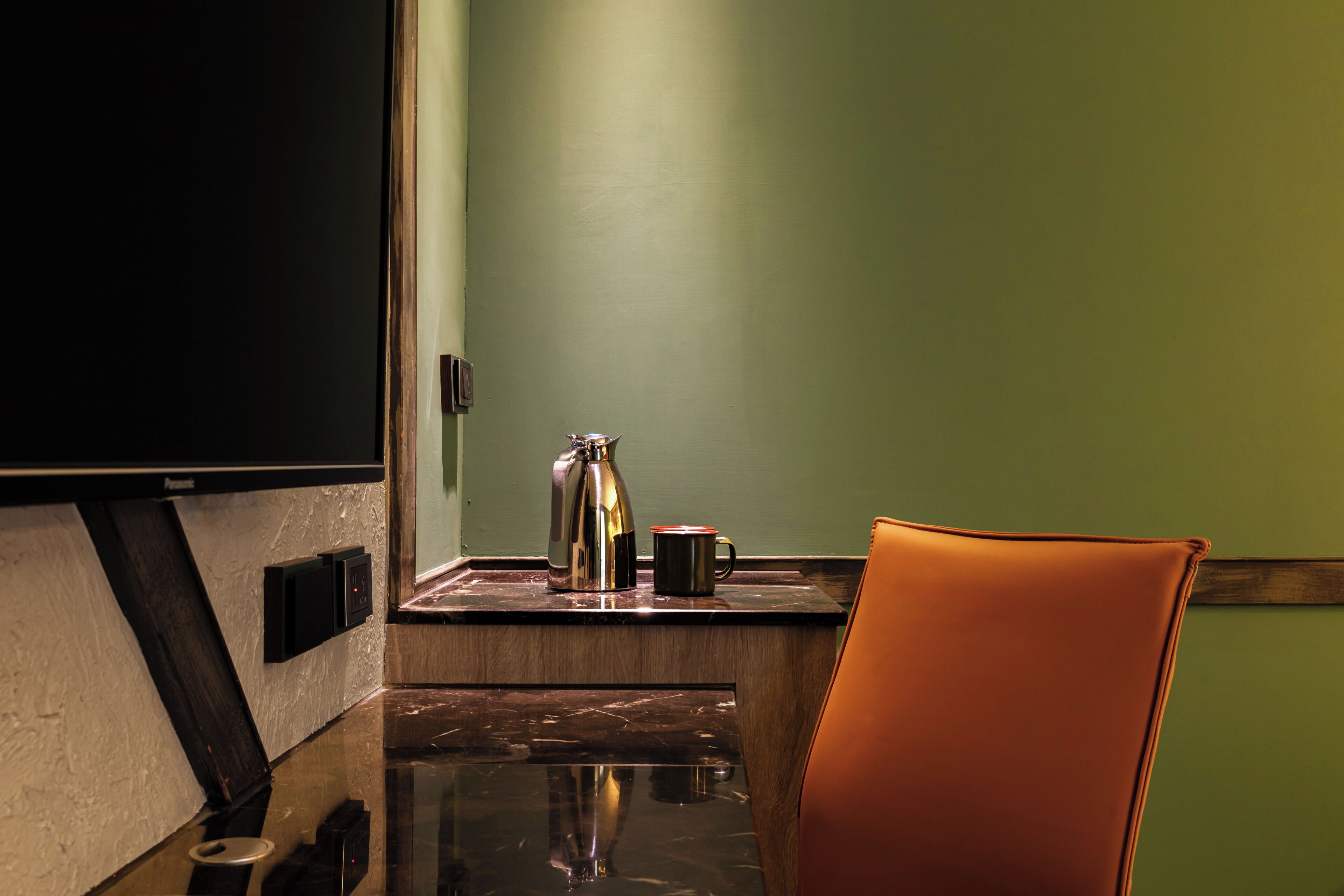 A room with a flat-screen TV, a coffee maker, a mug, and a leather chair.