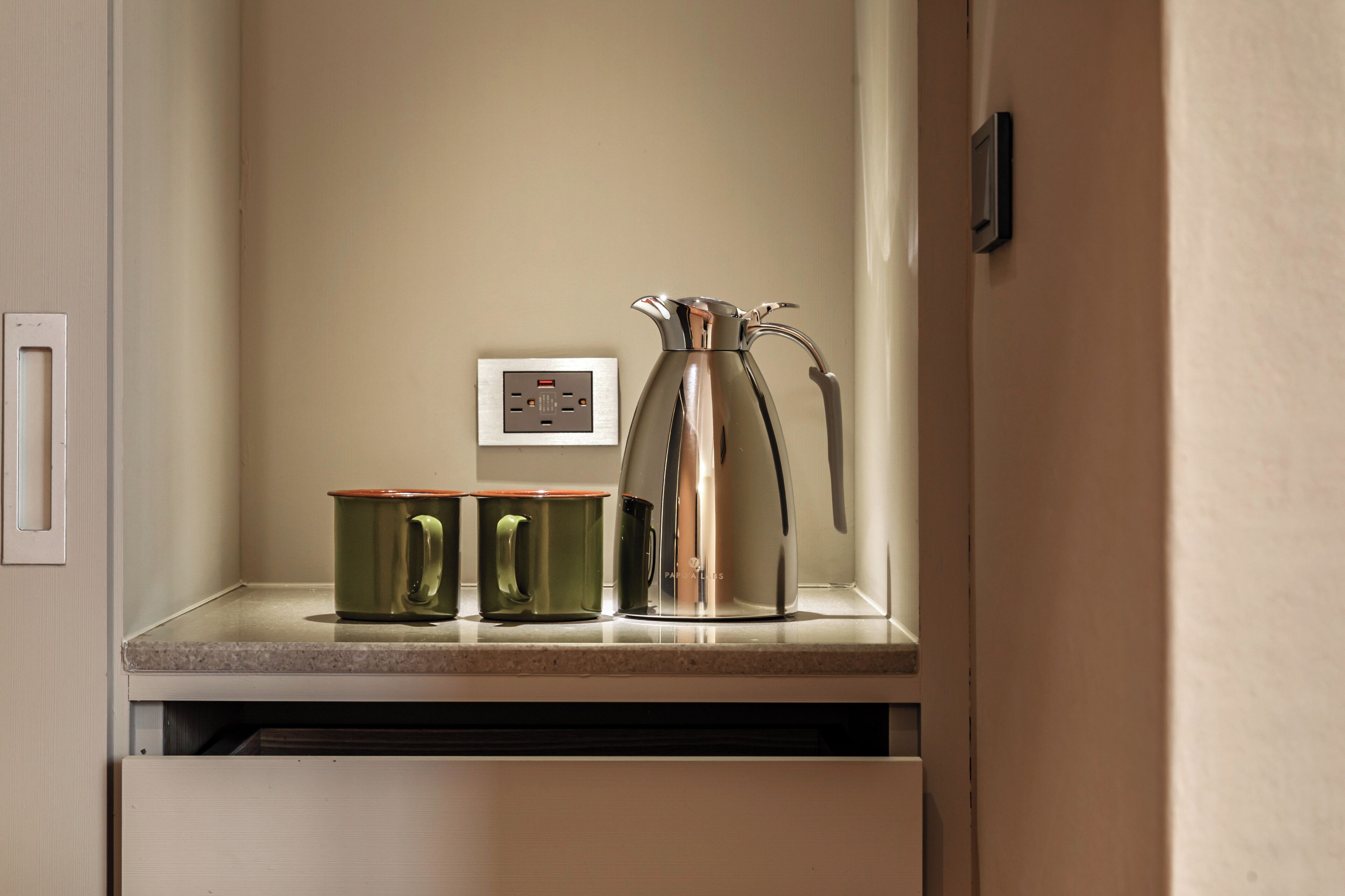 A kitchen counter with a coffee maker, two green mugs, and a power outlet.