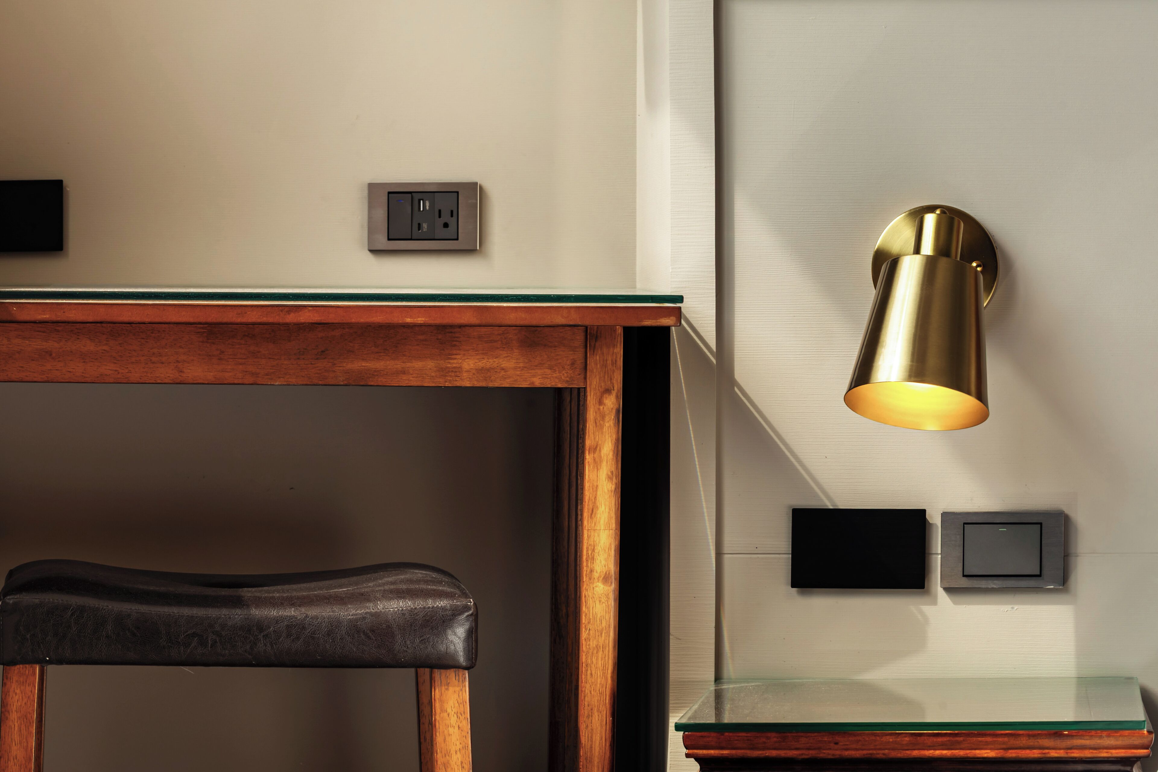 A wooden table with a bench, a wall-mounted light fixture, and two wall sockets.