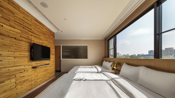 A hotel room with a wooden wall, a large window, two beds, a TV, and a city view. - LUXIAINN (Tainan)