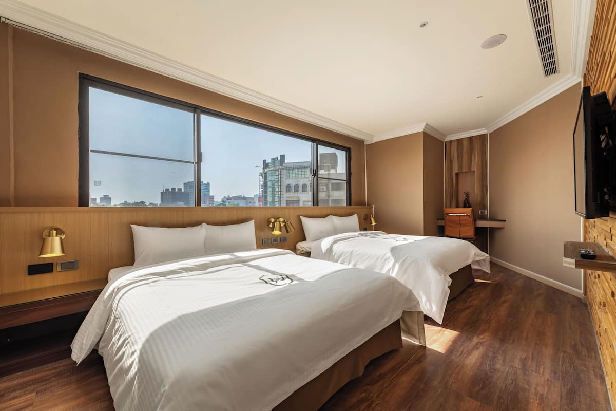 A hotel room with two beds, a large window, a wooden headboard, and a city view.