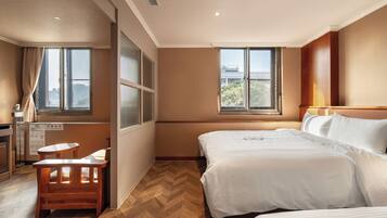 Ein Hotelzimmer mit zwei Betten, einem Schreibtisch, einem Stuhl und großen Fenstern mit Blick auf die Stadt.