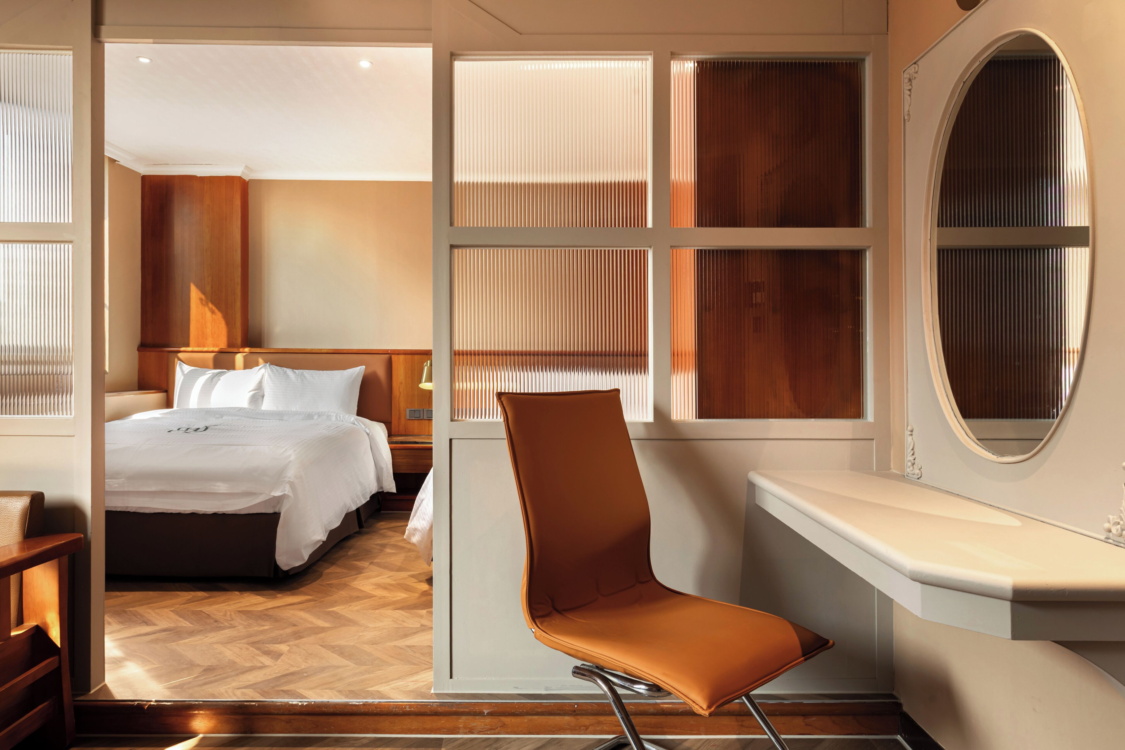Quarto de hotel com cama, cadeira, penteadeira e uma janela grande com persianas.