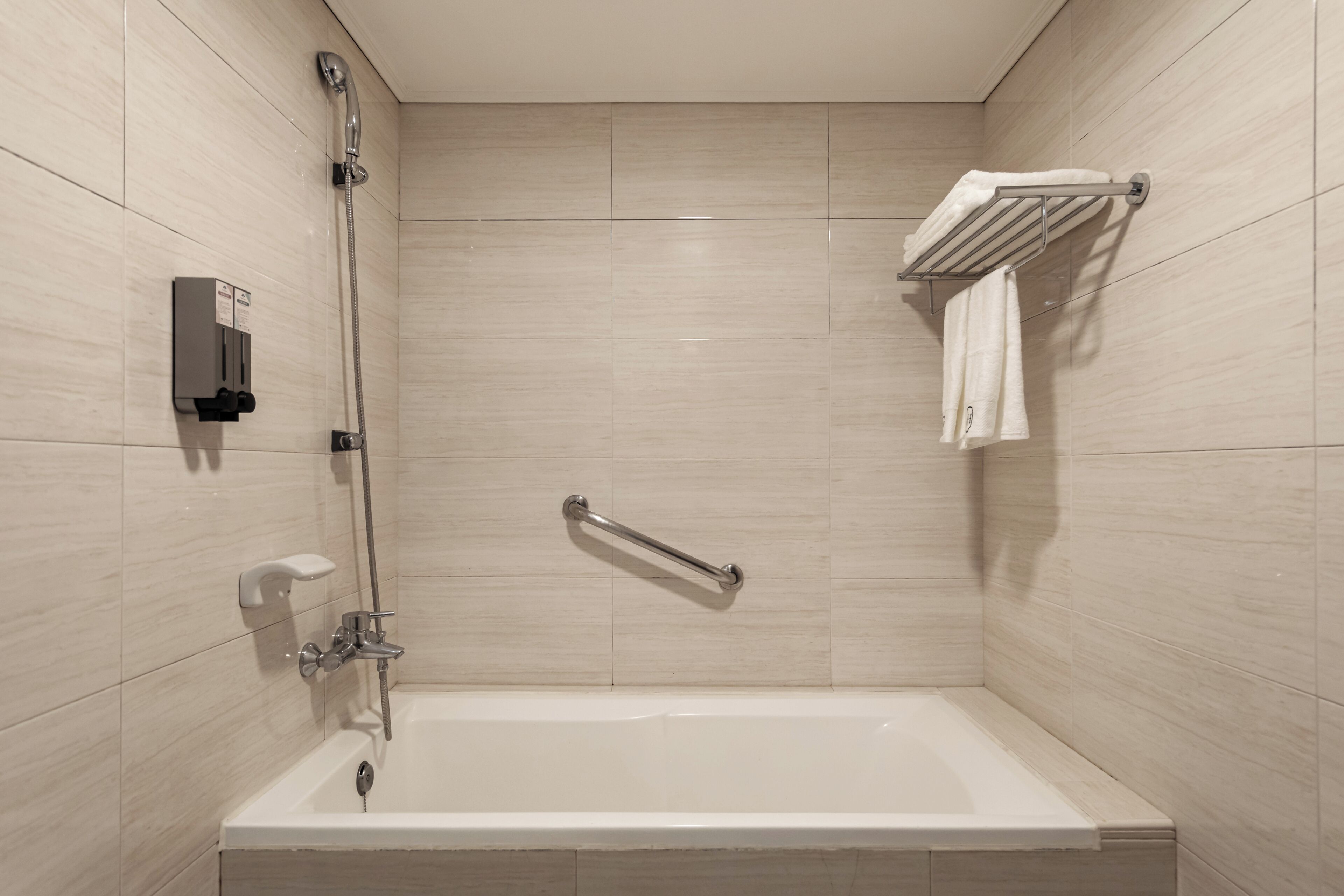 Une salle de bain moderne équipée d’une baignoire, d’un pommeau de douche à main, d’un porte-serviettes et d’un distributeur de savon.