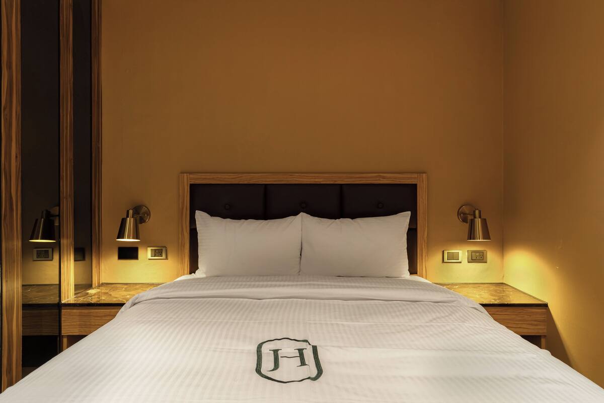 A hotel room with a large bed, two bedside lamps, a headboard, and a bedside table with a lamp.