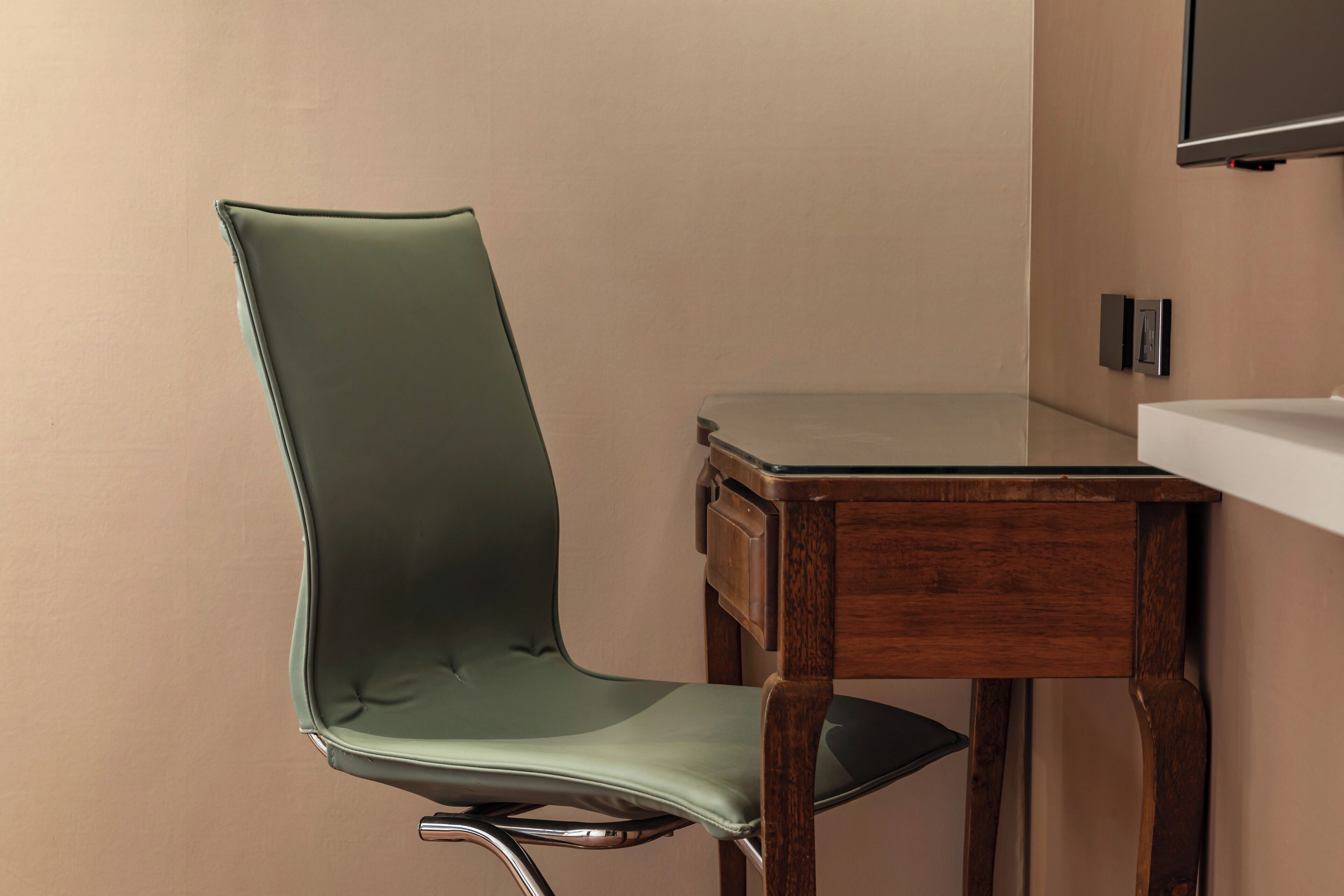 A chair with a metallic frame and a cushioned seat, positioned next to a wooden table with a drawer.