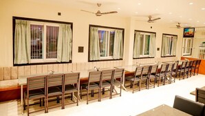 A dining area with multiple tables and chairs, ceiling fans, and windows with curtains.