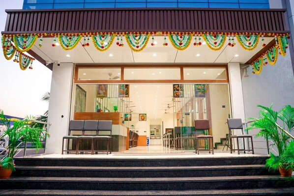 A hotel entrance with a covered outdoor seating area, glass doors, and steps leading up to the entrance. - Hotel Govind And Rooms (Chhatrapati Sambhajinagar)