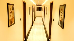 A hotel hallway with framed artwork on the walls, a marble floor, and doors leading to rooms.