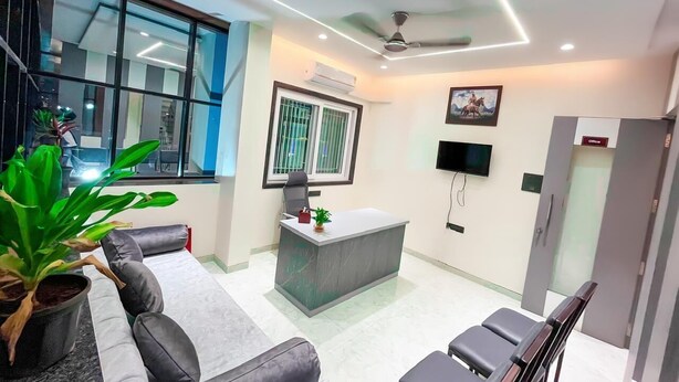 A modern office reception area with a reception desk, seating, a large window, and a ceiling fan.