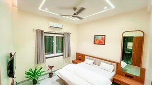 A bedroom with a bed, a ceiling fan, a window with curtains, a wall-mounted TV, and a mirror.