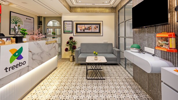 A reception area with a marble counter, a sofa, a coffee table, and a TV mounted on the wall. - Treebo Arizona (Gandhinagar)