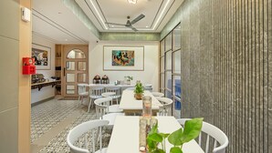 A modern dining area with white tables and chairs, a ceiling fan, and a decorative light fixture. - Treebo Arizona (Gandhinagar)