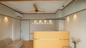 Un espace d’accueil avec un comptoir de réception en bois, un ventilateur de plafond et un climatiseur fixé au mur.