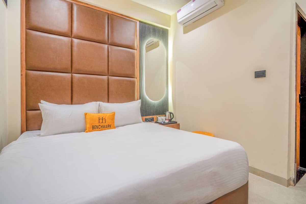 Une chambre d’hôtel avec un grand lit, une tête de lit à motifs rembourrés, une table de chevet avec une lampe et un appareil de climatisation fixé au mur.