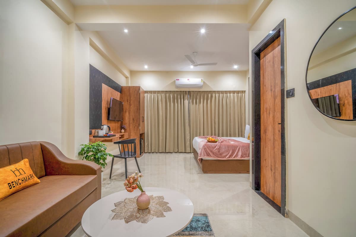 Une chambre d’hôtel moderne avec un canapé, une table basse ornée d’un vase, un lit recouvert d’une couverture rose, un bureau avec une chaise et un grand miroir.