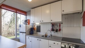 Eine kompakte Küche mit weißen Schränken, einem Einbauofen und einem Fenster mit Jalousien.